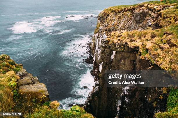waves breaking over rock formation at base of cliff at látrabjarg - halbinsel stock-fotos und bilder