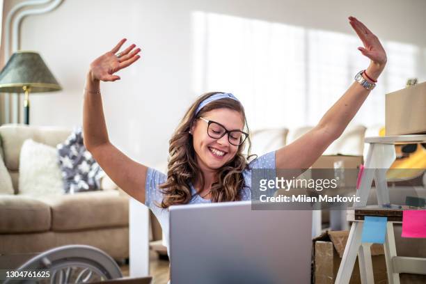 young woman moving to a new apartment. a young beautiful woman sitting on the floor in a new house. a portrait of a happy woman who is in her new home unpacking things out of boxes. - student flat stock pictures, royalty-free photos & images