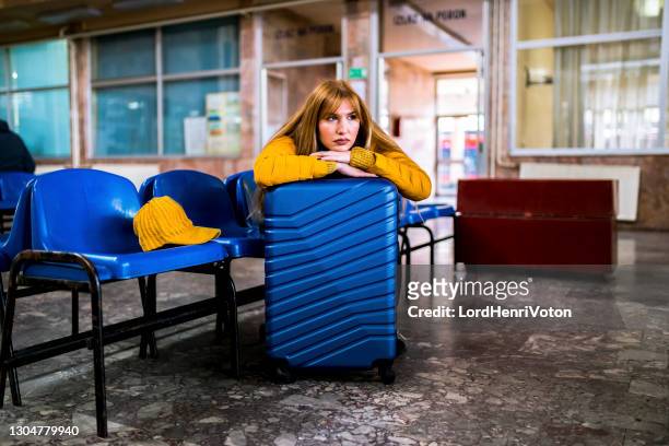 young woman with suitcase sitting bored at train station - holiday sadness stock pictures, royalty-free photos & images