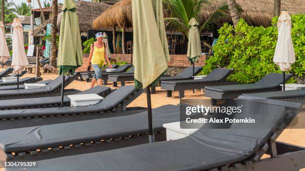 positive, happy european woman, a tourist, is walking on a tropical beach between unoccupied chaise-lounges - chaise longue stock pictures, royalty-free photos & images