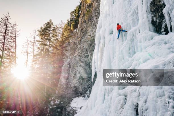 bright sunrise with ice climber ascending a tall frozen waterfall as sun crests above the horizon - 38 north stock-fotos und bilder