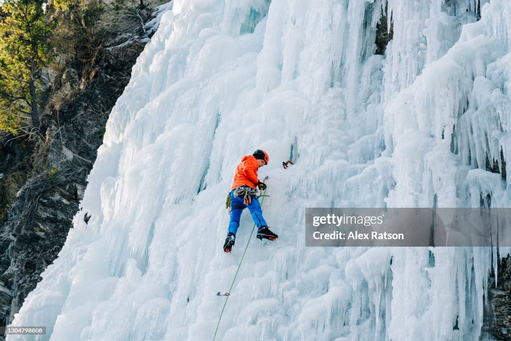 Ice climber clips his climbing rope to a ice screw while high up on a frozen waterfall