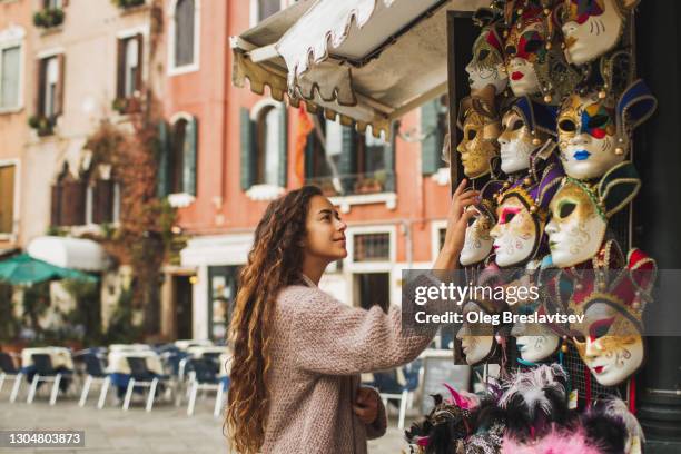 tourist woman choosing venetian mask on street stall in italy. traditional souvenir from venice - souvenir stock-fotos und bilder