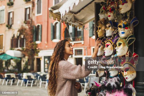 Tourist woman choosing Venetian mask on street stall in Italy. Traditional souvenir from Venice