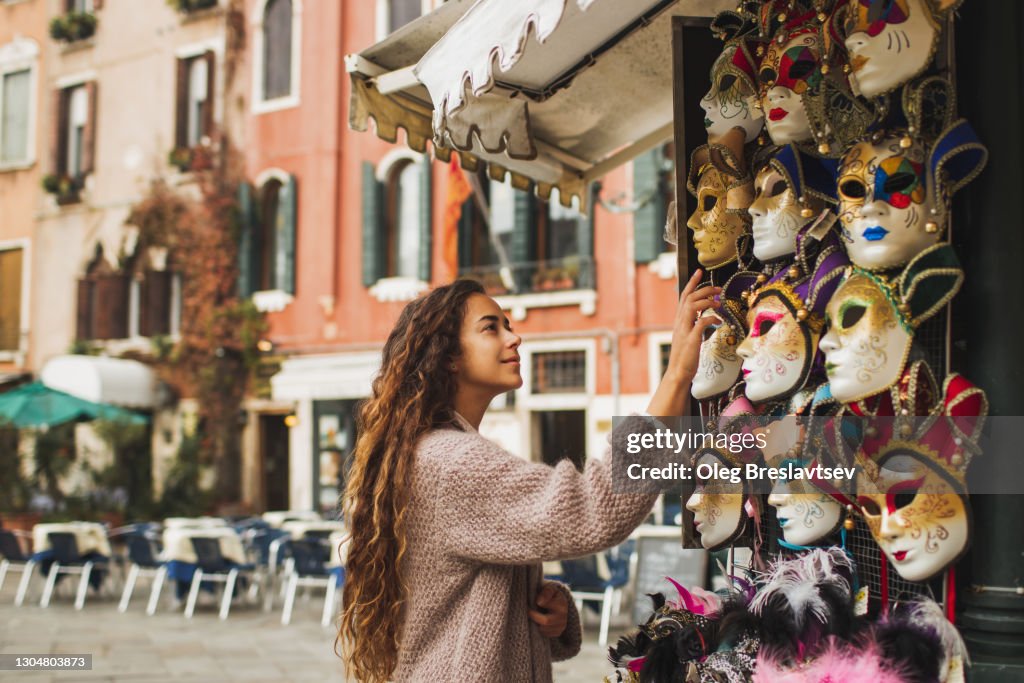 Tourist woman choosing Venetian mask on street stall in Italy. Traditional souvenir from Venice