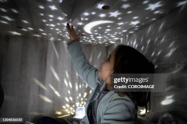 child with a night lamp projecting stars and moon at bedroom. - niño en la sala con juguetes fotografías e imágenes de stock