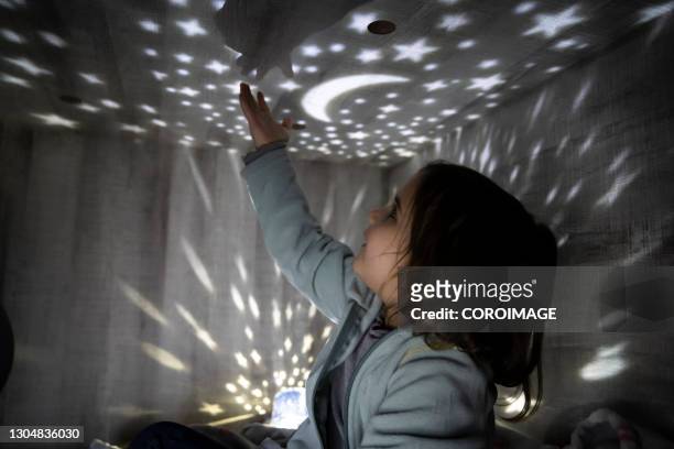 child with a night lamp projecting stars and moon at bedroom. - chambre bébé photos et images de collection