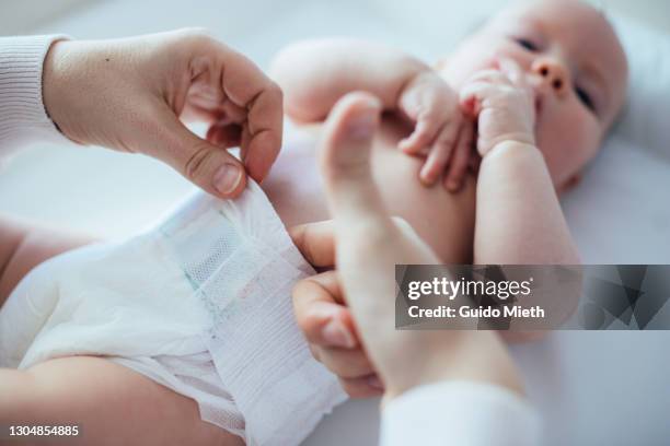 mother testing if diaper is too tight after changing. - nappy change stockfoto's en -beelden