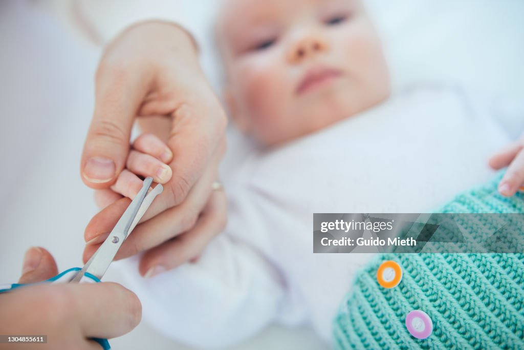 Mother cutting finger nails of her baby girl.