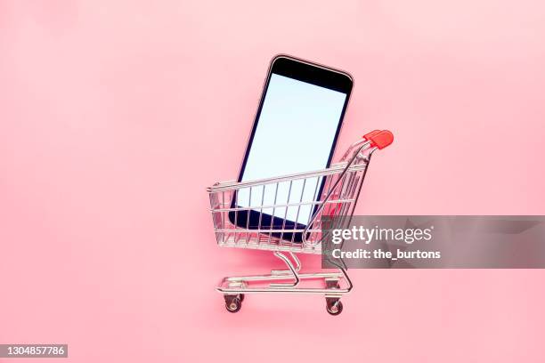small empty shopping cart and mobile phone on pink background, online shopping - chariots et charrettes photos et images de collection