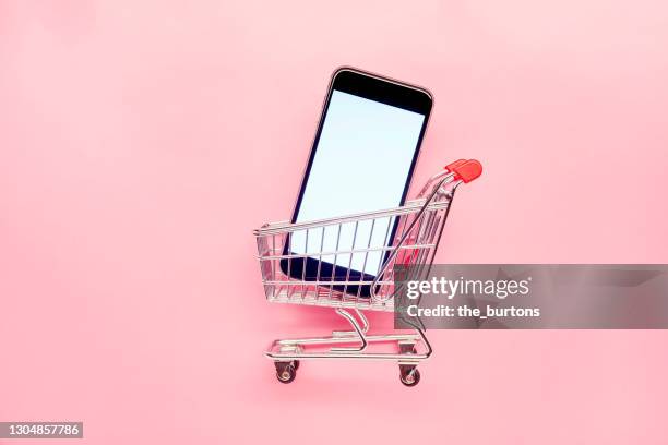 small empty shopping cart and mobile phone on pink background, online shopping - ホームショッピ�ング ストックフォトと画像