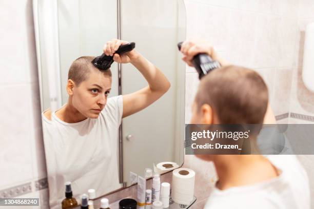 survivante de cancer dans la salle de bains rasant ou coupant ses cheveux - woman shaving her head photos et images de collection
