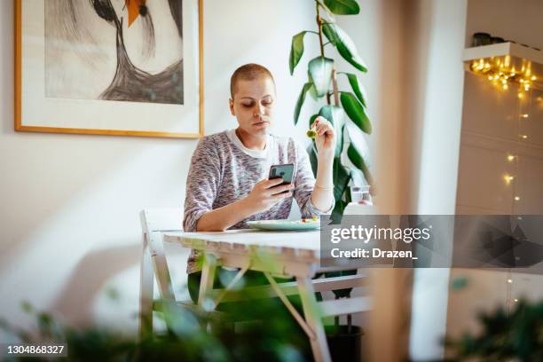 cancer cured woman using phone while eating lunch at home - cellphone cancer illness stock pictures, royalty-free photos & images