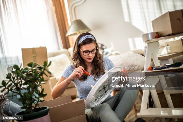 joven que se muda a un nuevo apartamento. una joven hermosa mujer sentada en el suelo en una casa nueva. un retrato de una mujer feliz que está en su nuevo hogar desempacar las cosas de las cajas. - reloj de pared fotografías e imágenes de stock