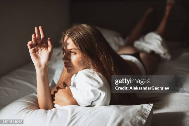 mujer protegiendo su mirada de rayos solares mientras se acuesta en la cama - tanga fotografías e imágenes de stock