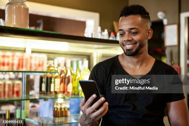 lächelnder junger mann schaut auf handy in spirituosen-shop - beer fridge stock-fotos und bilder