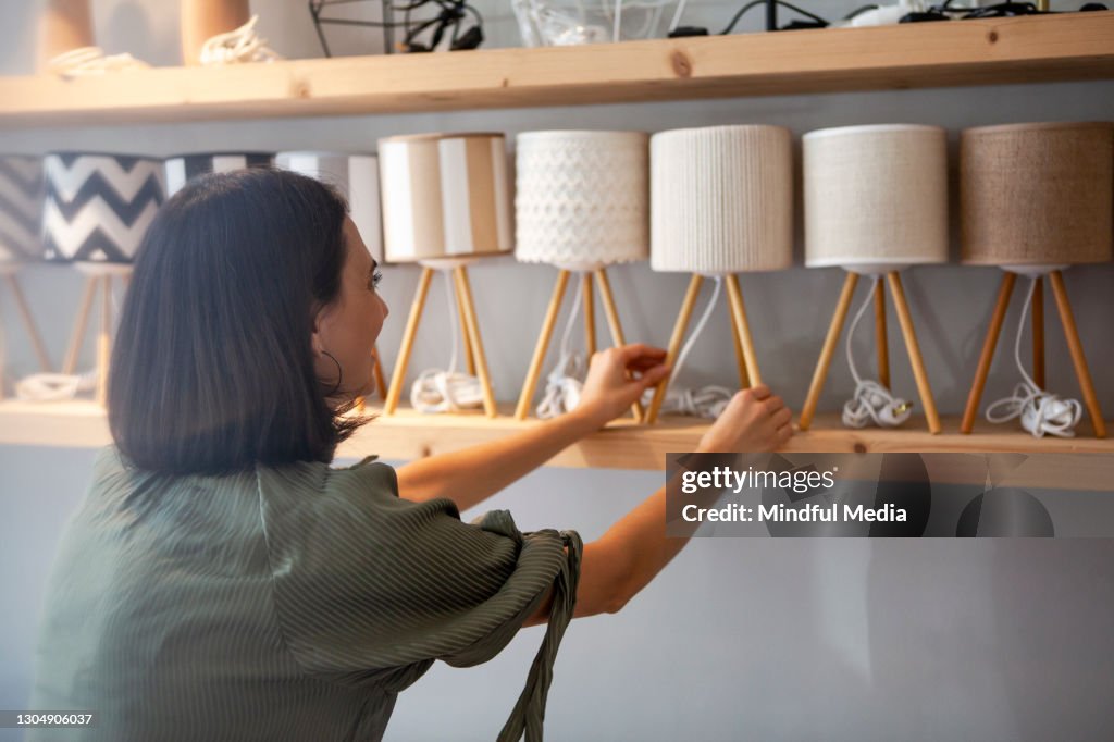 Portrait of young adult woman arranging night table lamps at deco store