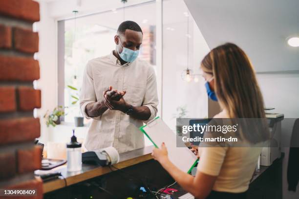 businessman disinfects his hands at hotel reception, covid-19 pandemic - reception desk stock pictures, royalty-free photos & images