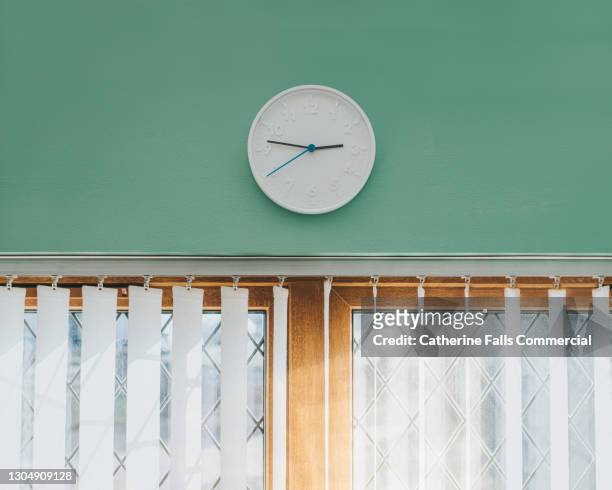 a simple white wall clock above a sunny window, in the afternoon - wandklok stockfoto's en -beelden