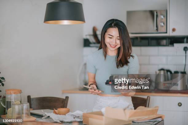 belle femme chinoise asiatique recevant le déballage essayant sur son casque des achats en ligne à la cuisine - new stock photos et images de collection