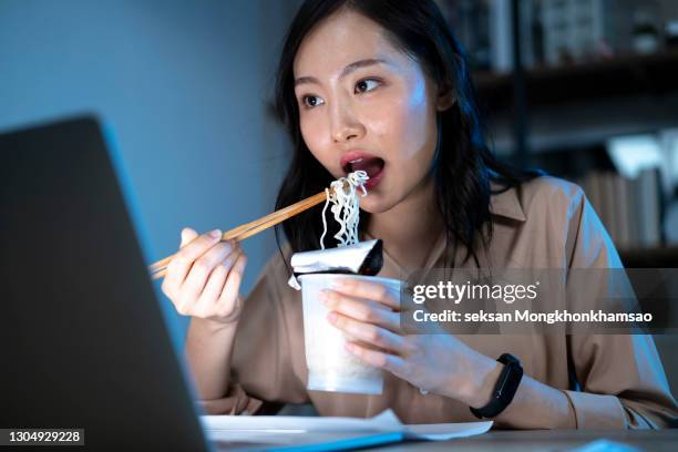 asia freelance smart business women eating instant noodles while working on laptop in living room at home - telecommuting eating stock pictures, royalty-free photos & images