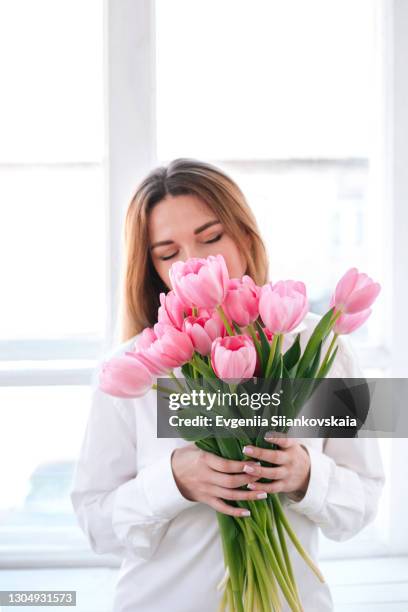 young beautiful woman with pink tulips near the window. - tulpen stock-fotos und bilder