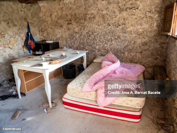 dirty room in ruins, with a mattress and kitchen equipment invaded by squatters. - hut interior stock pictures, royalty-free photos & images