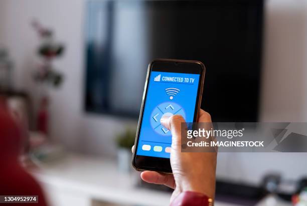 rear view of woman using phone app while watching smart tv at home - remote controlled fotografías e imágenes de stock
