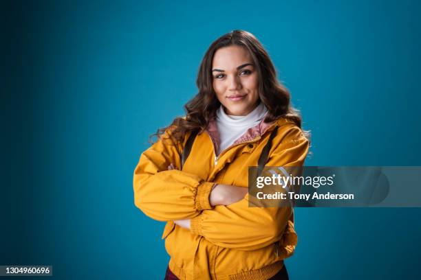 portrait of young mixed race woman on blue background - yellow jacket stock pictures, royalty-free photos & images