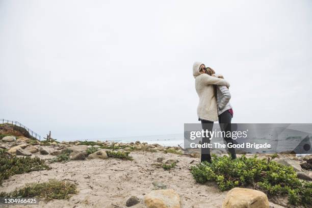 mother embracing daughter at beach against clear sky - hugging mid section stock pictures, royalty-free photos & images