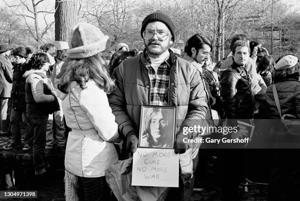 View of a fans, who holds a photo of musician John Lennon and a sign, in Central Park at a memorial vigil following Lennon's murder, New York, New...