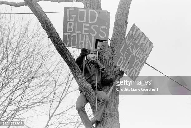 View of a fan who holds two signs while perched in a tree near the Central Park bandshell during a memorial vigil for murdered musician John Lennon,...