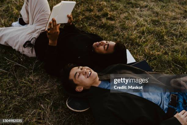 young man reading diary lying down by male friend on grass in park - friends male stock-fotos und bilder