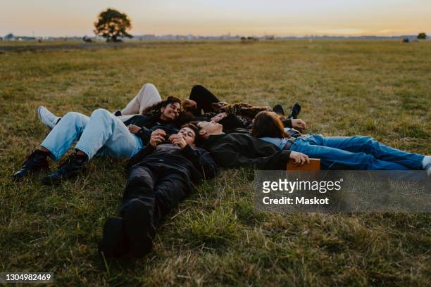 young male and female friends lying on grass in park - menschengruppe stock-fotos und bilder