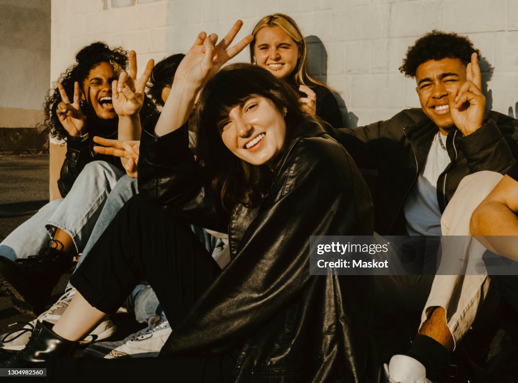 Portrait of smiling friends doing peace sign against wall