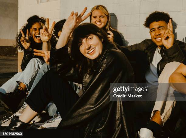 portrait of smiling friends doing peace sign against wall - victory sign man stock-fotos und bilder