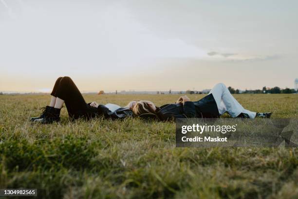 female friends lying down on grass in park - laying park stock pictures, royalty-free photos & images