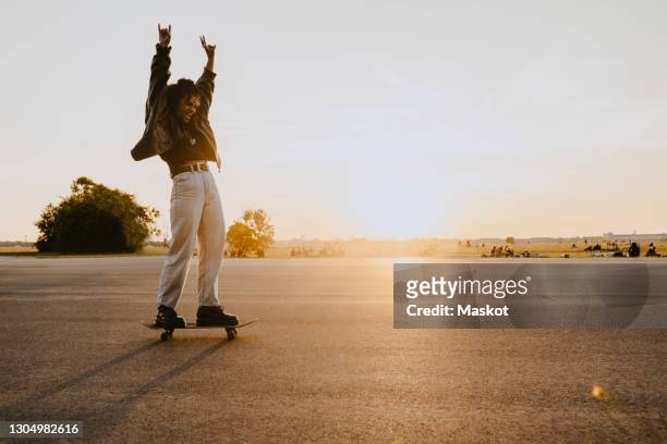 cheerful woman with hand raised skating on road in park - women skateboarding stock pictures, royalty-free photos & images