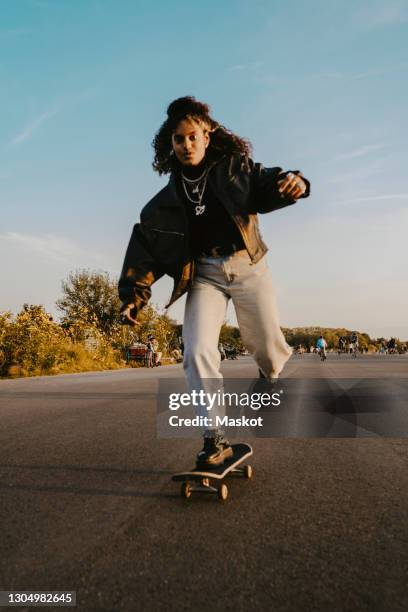 portrait of cheerful woman skating on road in park - monopatín actividades recreativas fotografías e imágenes de stock