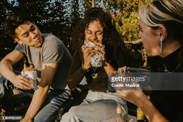 young woman eating food with friends in park - generation z food stock pictures, royalty-free photos & images