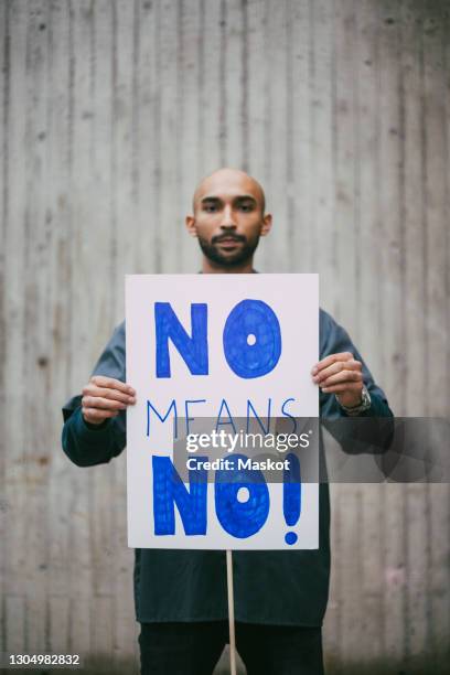 portrait of male activist holding no means no poster against against wall - protester sign stock pictures, royalty-free photos & images