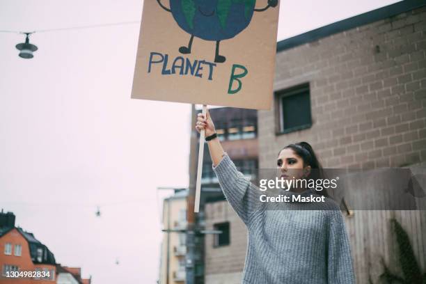 female activist looking away while holding planet earth poster during social movement - social justice concept stock pictures, royalty-free photos & images