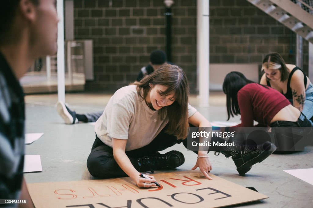 Smiling woman preparing signboard while sitting with male and female activists in building