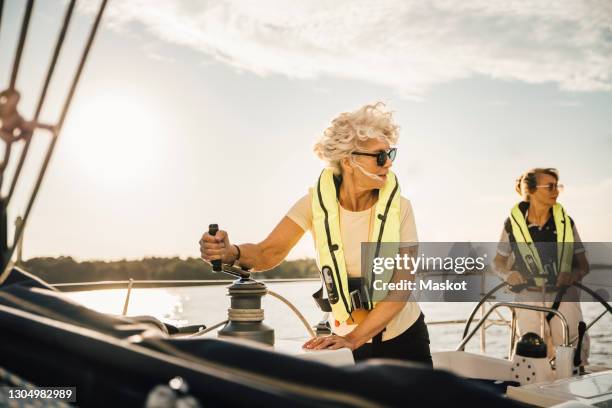 female friends looking away while sailing in boat against sky - life jacket photos stock pictures, royalty-free photos & images