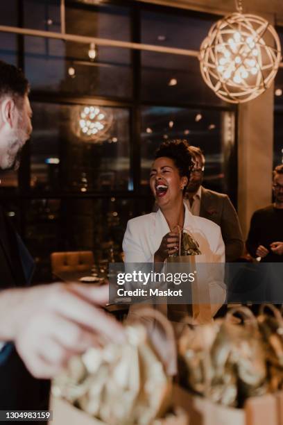 cheerful businesswoman laughing while holding gift bag at office party - work party stock pictures, royalty-free photos & images