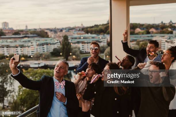 cheerful male and female colleagues taking selfie on smart phone during party in office - kick off call stock pictures, royalty-free photos & images