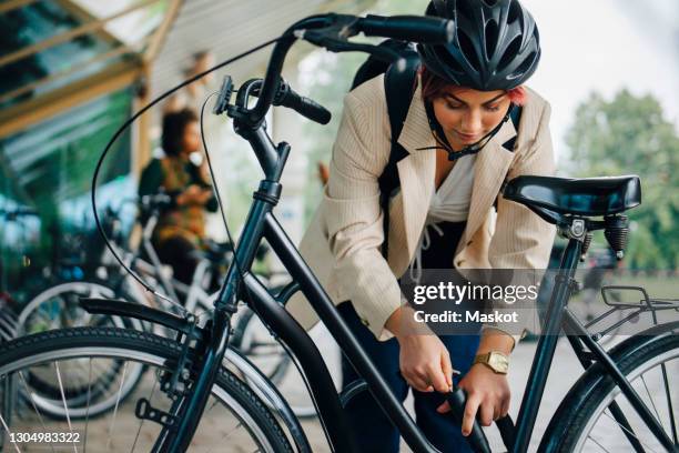 female student unlocking bicycle at parking station in college campus - bicycle parking station stock pictures, royalty-free photos & images