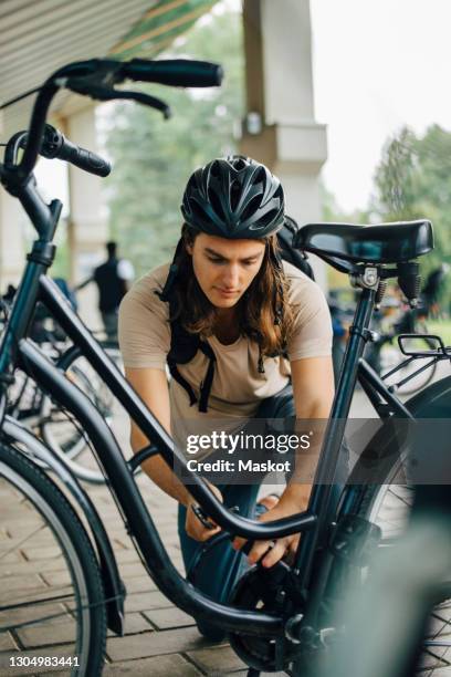 male student unlocking bicycle at parking station in college campus - bicycle parking station stock pictures, royalty-free photos & images