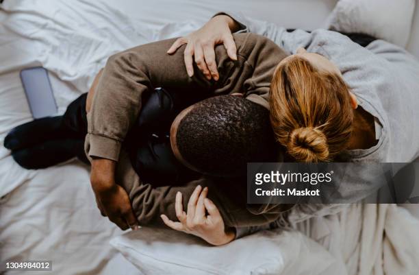 directly above shot of mother embracing depressed son on bed at home - man and woman cuddling in bed stockfoto's en -beelden