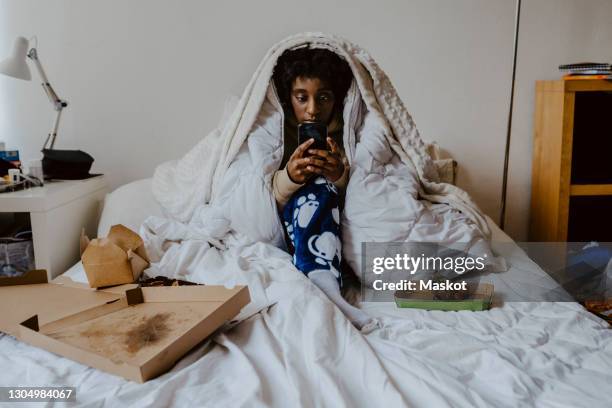 young woman using smart phone while sitting in bedroom - eating disorder stock pictures, royalty-free photos & images